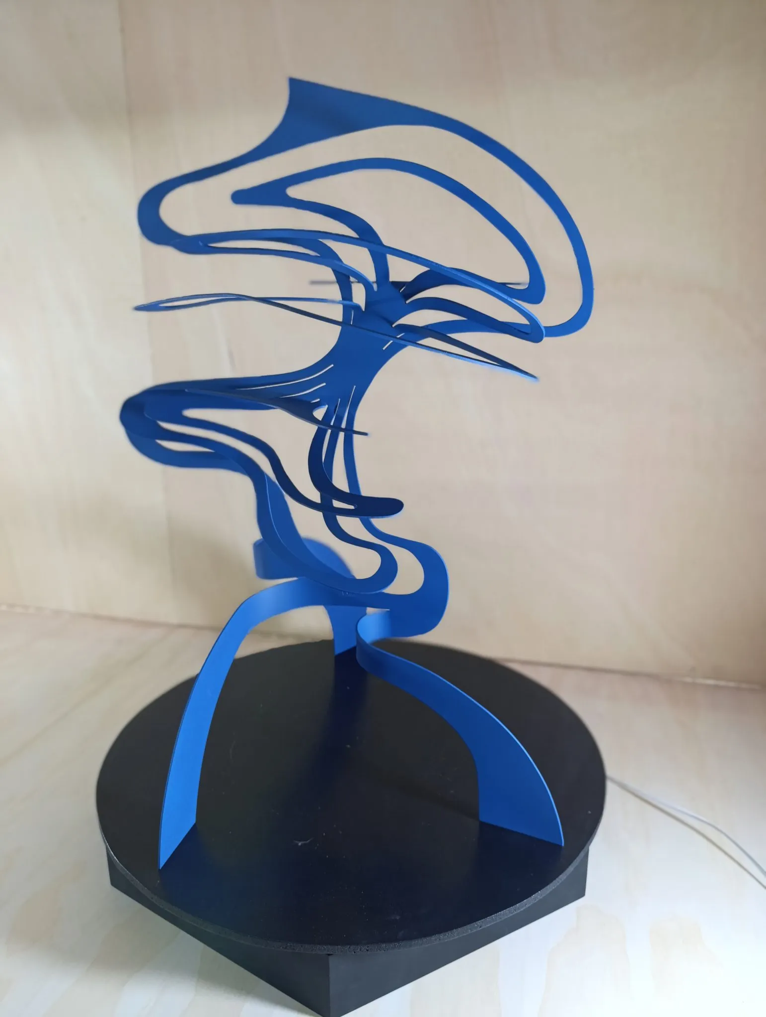 Blue painted iron ribbon sculpture spiraling upward from a black base